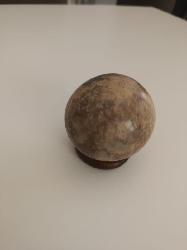 Sphère de dorodango mate, texture grise irrégulière, posée sur un socle en bois — un dorodango avant le travail de polissage